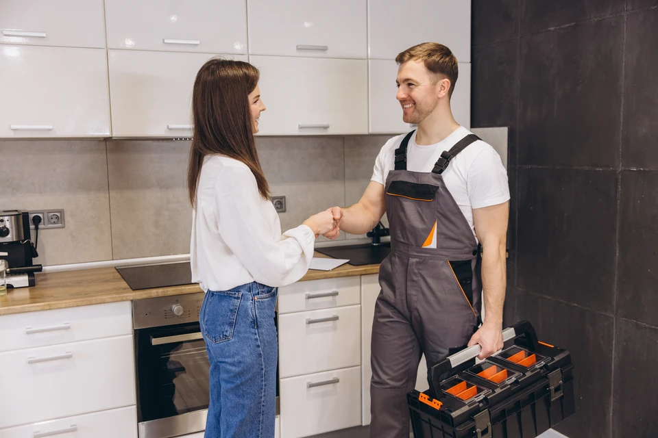 Plombier en salopette bleue réparant la plomberie sous un lavabo de salle de bain, allongé au sol avec des outils